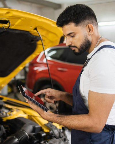 Serious focused man car technician mechanic repairing car problem of engine, during system checking